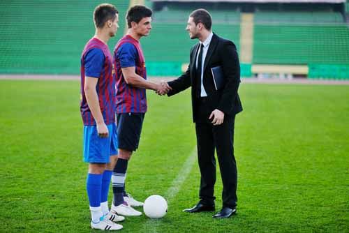 An Athlete Agent shakes hands with soccer players on a soccer field.